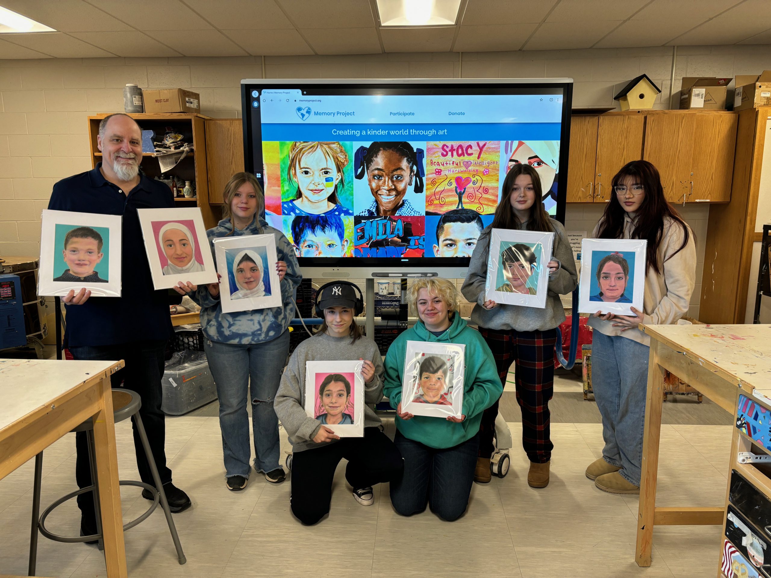 Five students and one teacher stand together holding painted portraits.