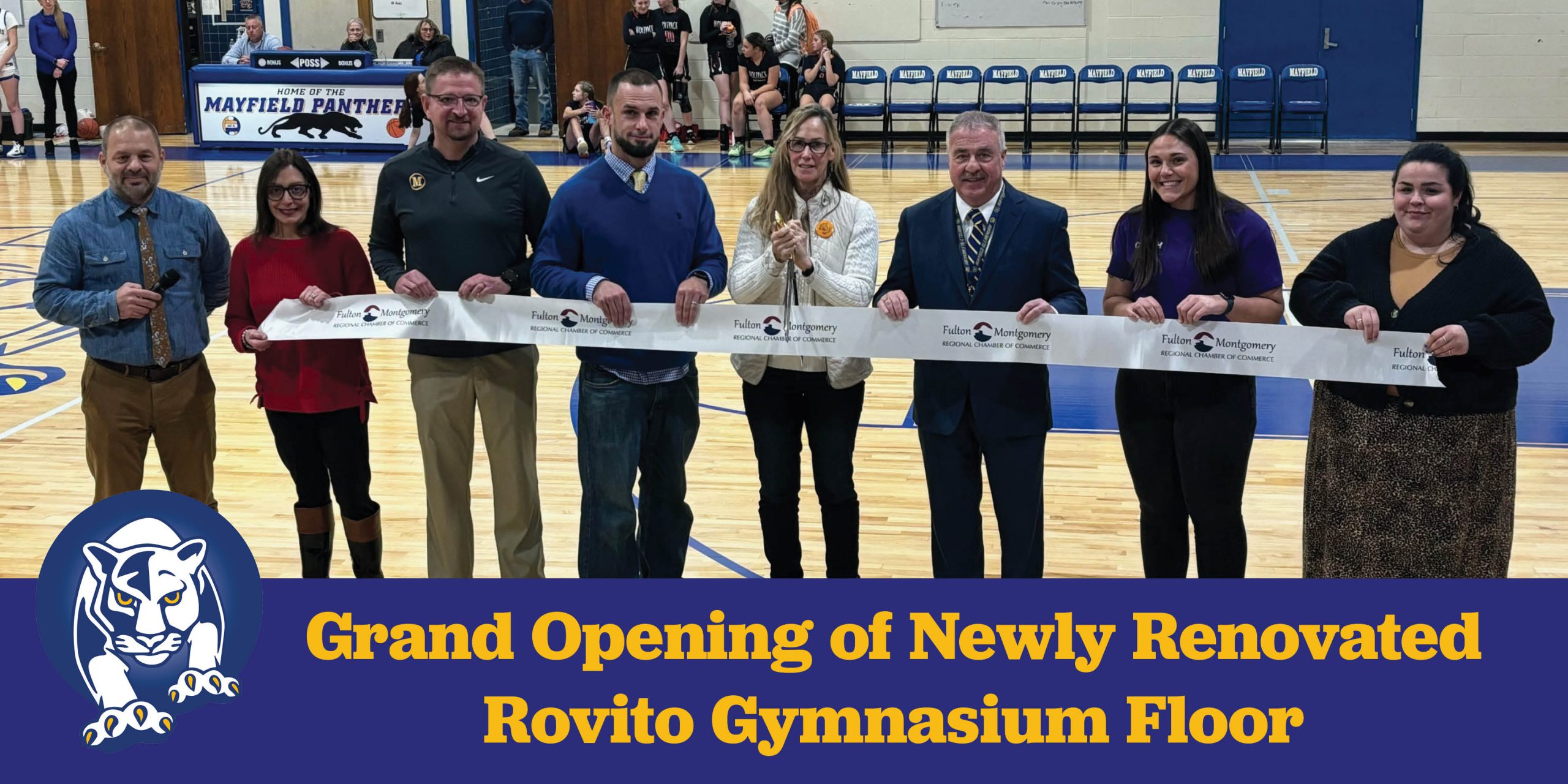 Eight people stand in a line in front of a ribbon and smile; woman in the middle holds big scissors over the ribbon. Panther logo is below and words: Grand Opening of the newly renovated Rovito Gymnasium floor.