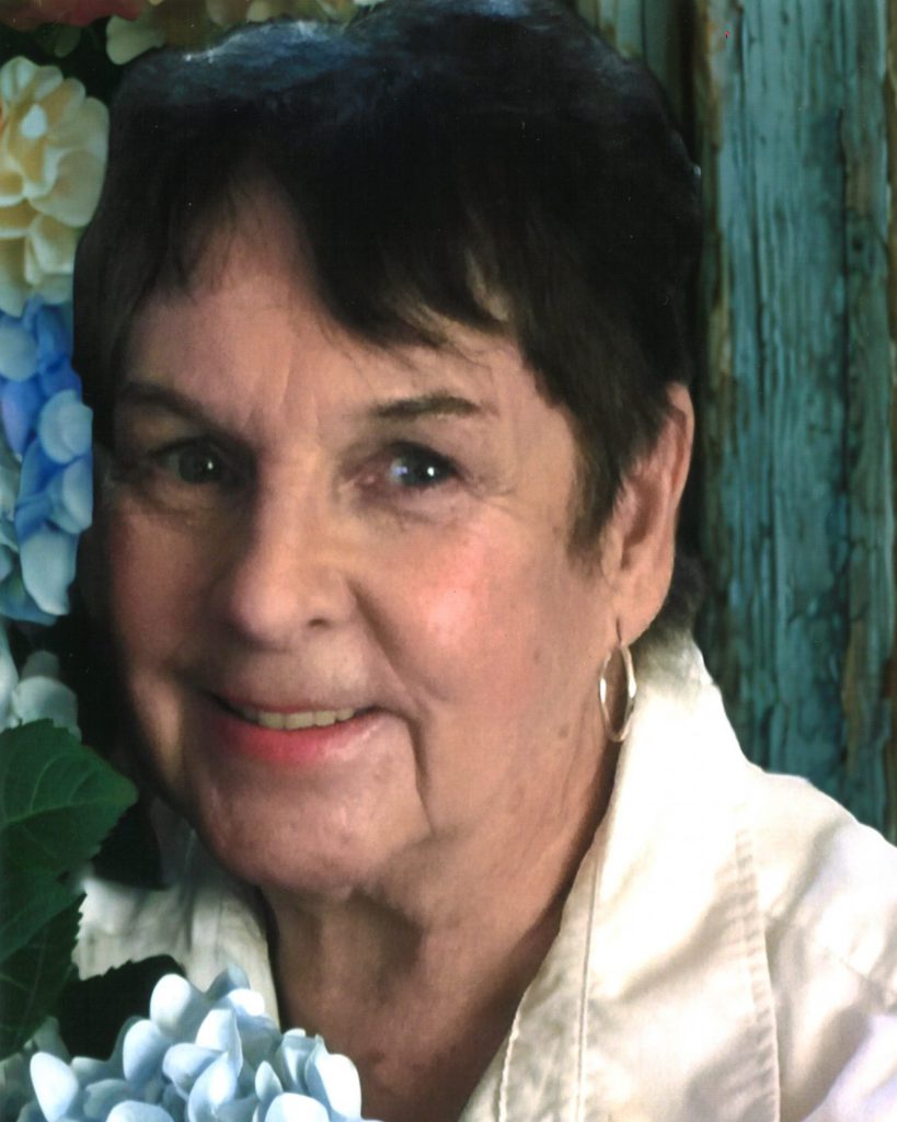 Headshot of Brunetto smiling next to flowers on wall.