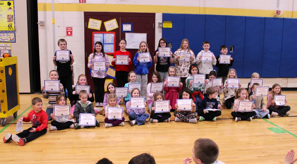 students sit in three rows and hold certificates