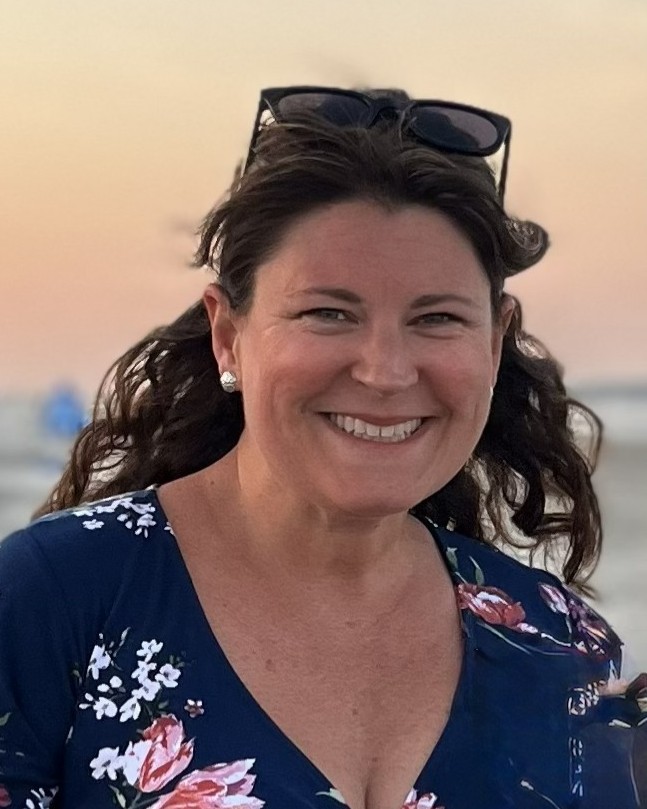 woman smiling wearing a blue flowered dress and sunglasses on her head