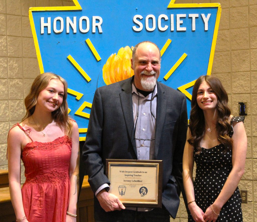 Two students stand with a teacher holder a plaque