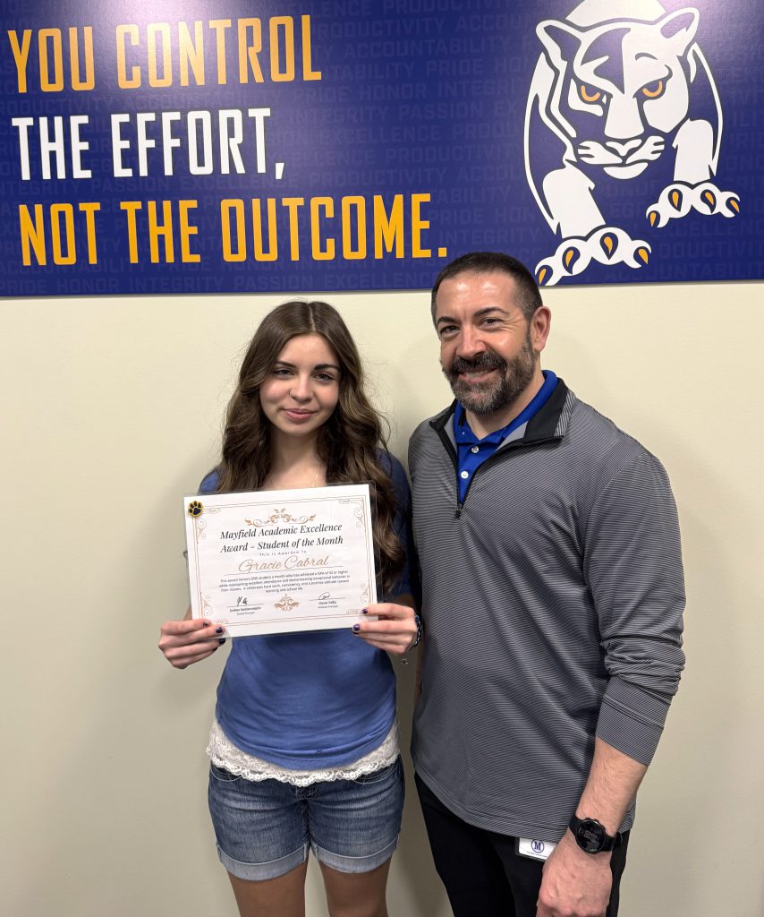 student holding a certificate stands with principal in front of a sign that says you control the effort, not the outcome