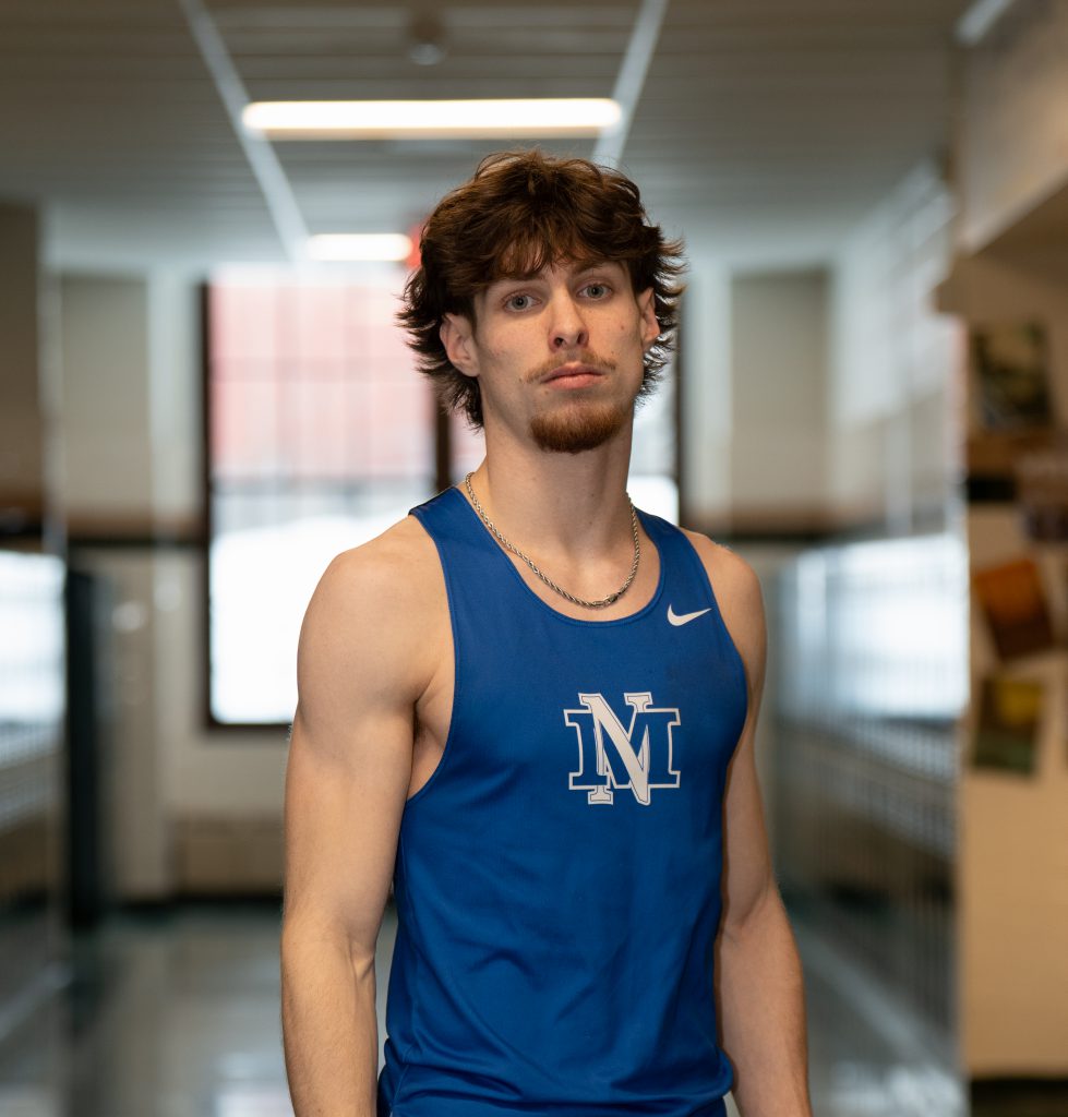 student in a track uniform stands in a hallway