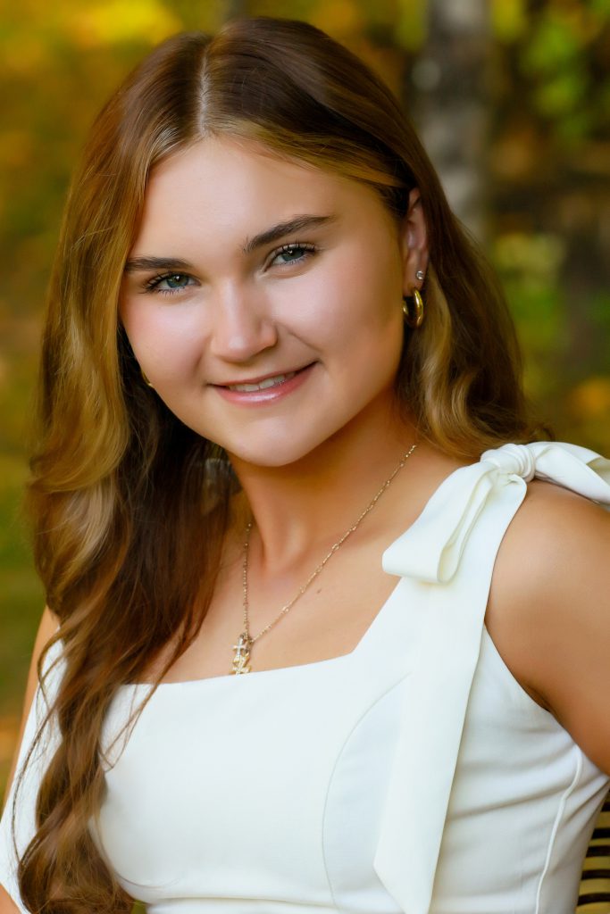 student in white in front of a tree background