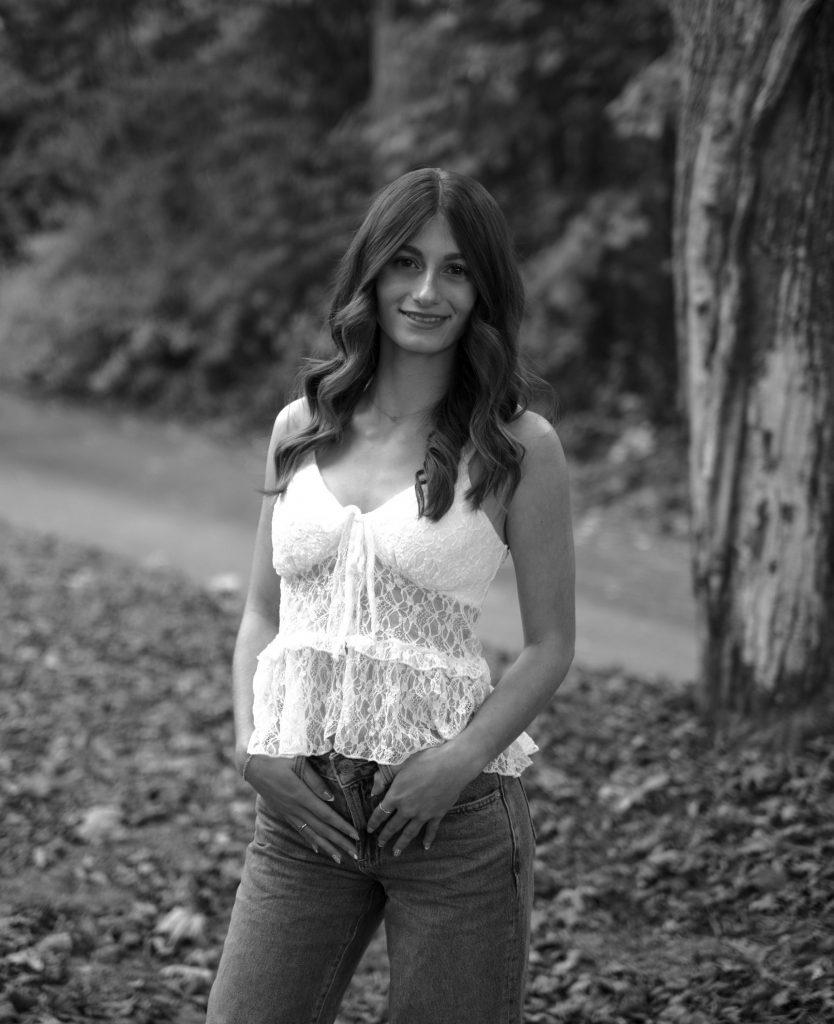 student in white standing in a forest
