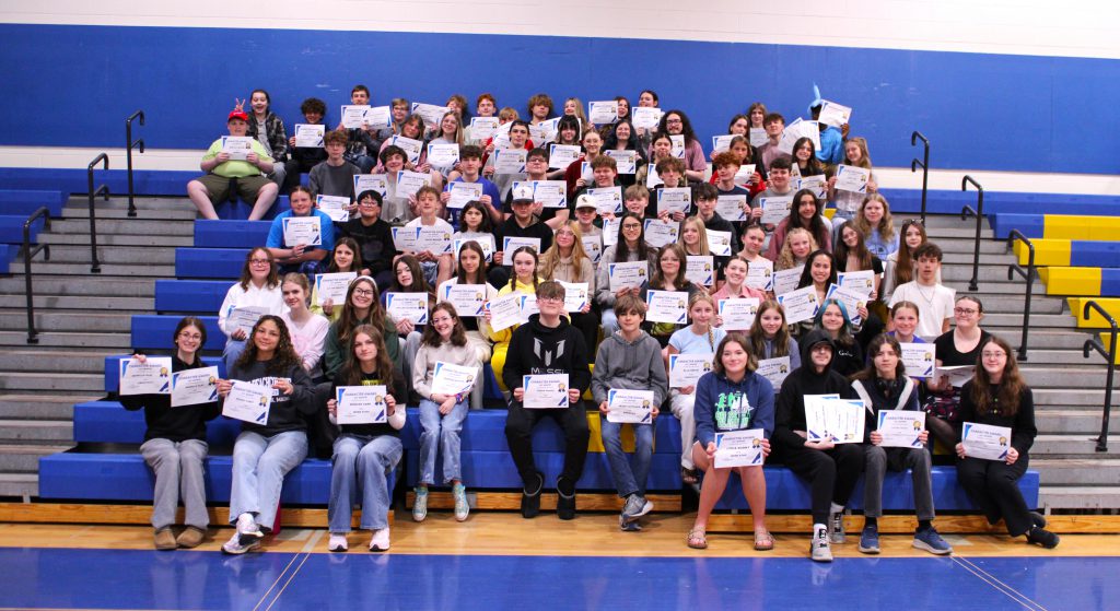 students sit on bleachers holding certificates