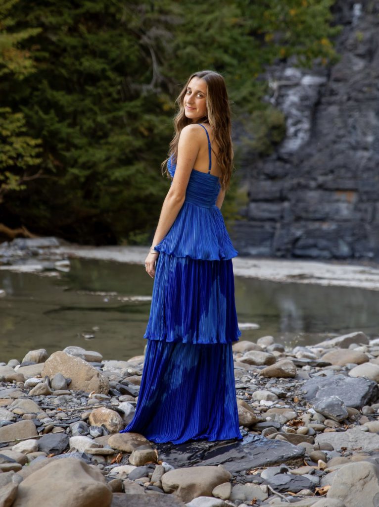 student in blue dress in front of a stream and trees