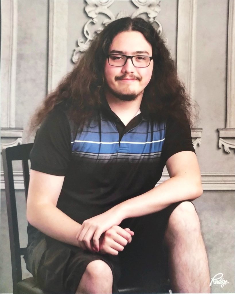 student with black and blue striped shirt sits in front of a scrolled backdrop