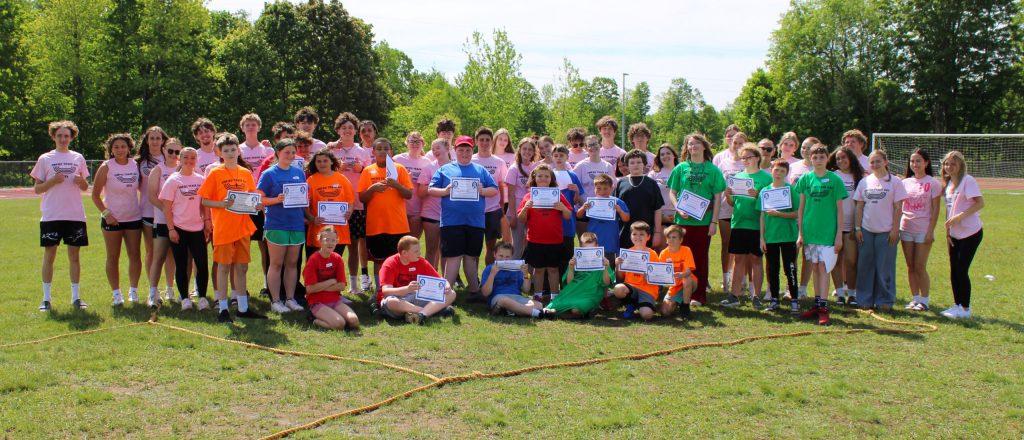 Group of students stand on a track field and hold certificates