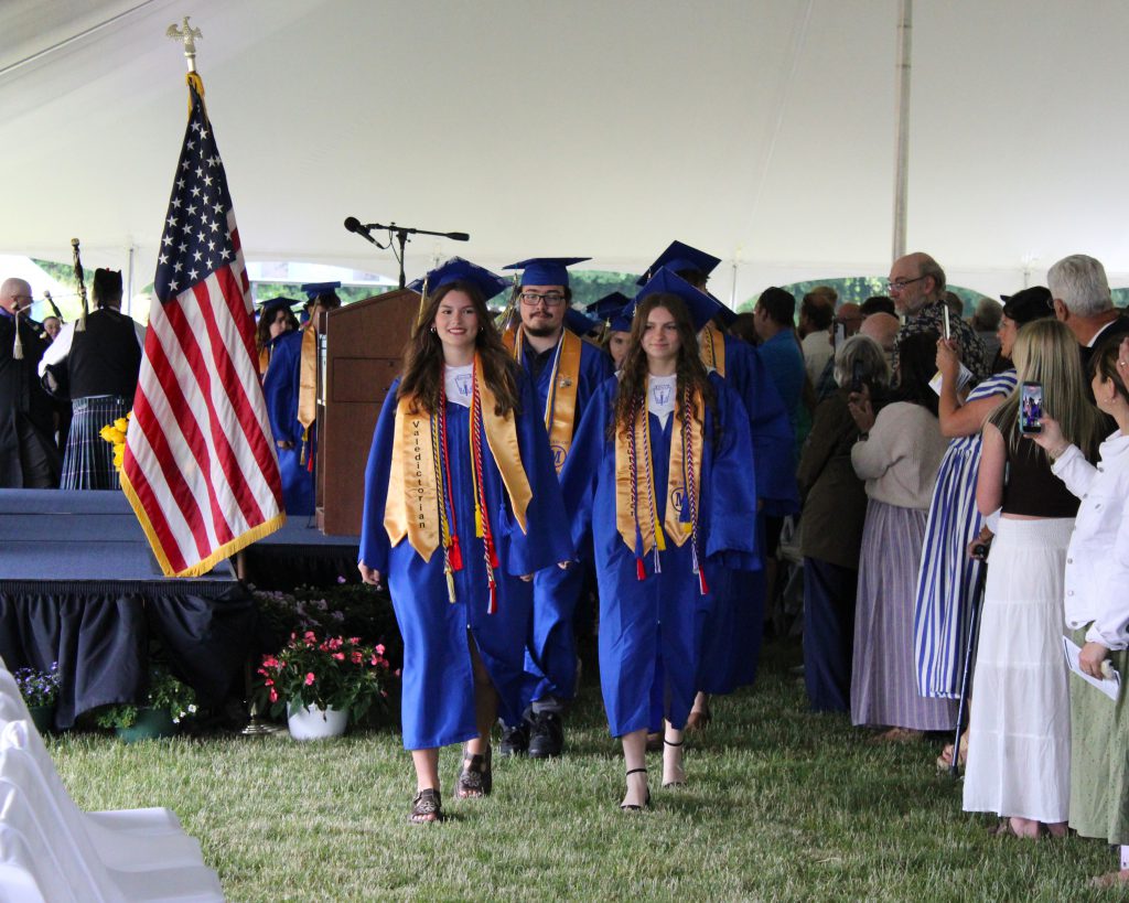Graduates walk into the tent with a crowd watching