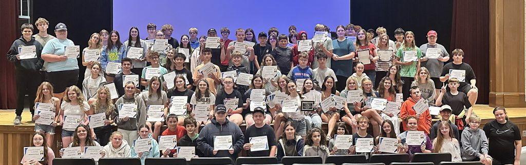 Rows of students stand on a stage and hold certificates