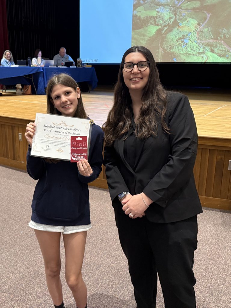A student holding a certificate stands with a teacher
