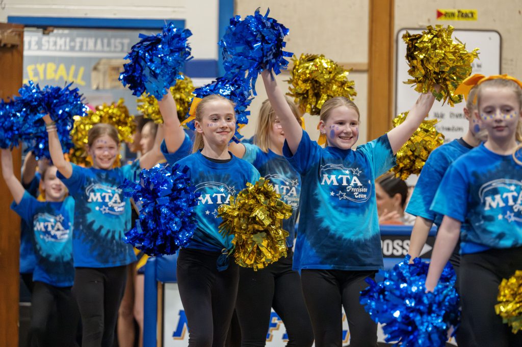 young cheerleaders wear matching shirts and hold up pompoms while smiling
