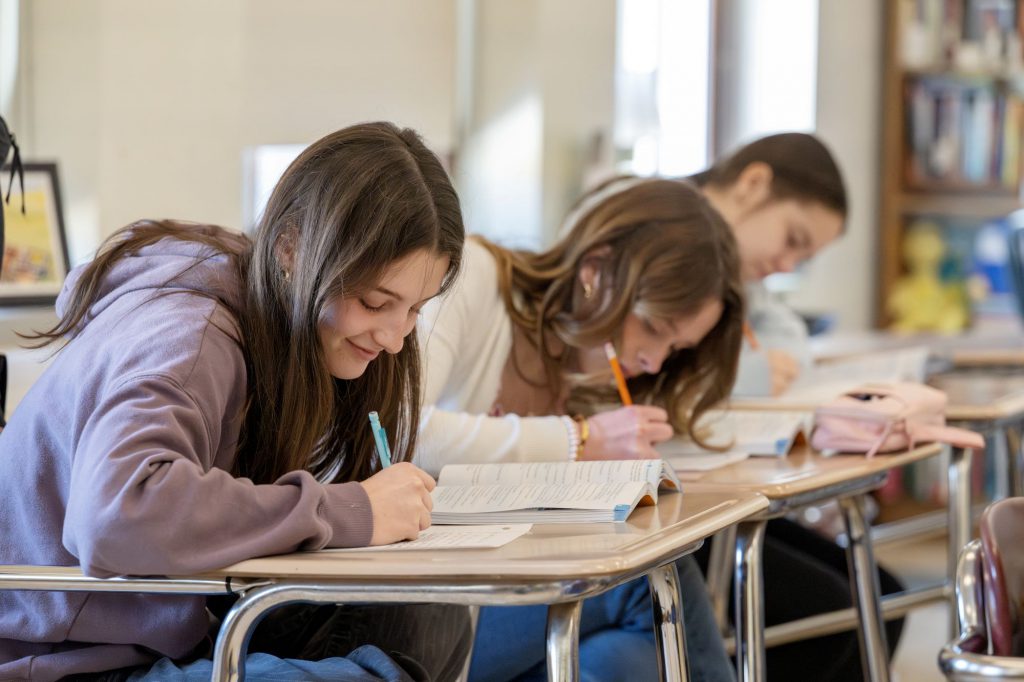 Three students sit at a desk and write