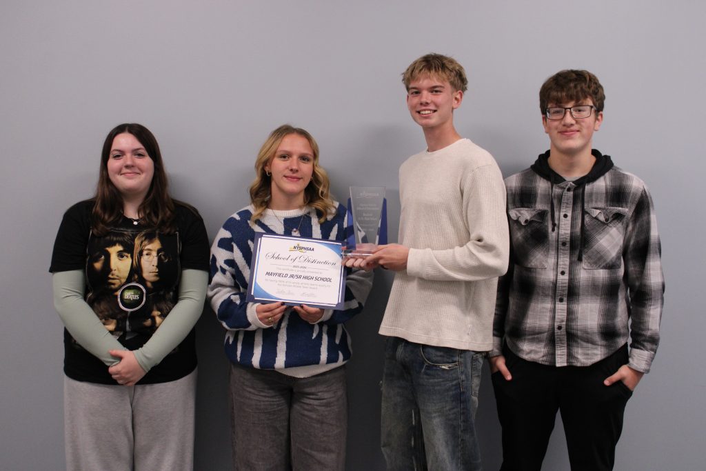 Four students stand together holding a glass award and certificate