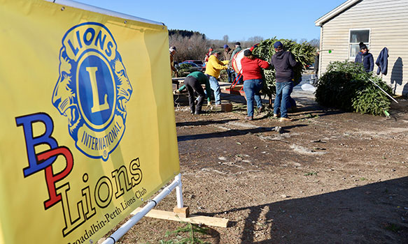 Lions Club sign with students and adults working with trees in the background