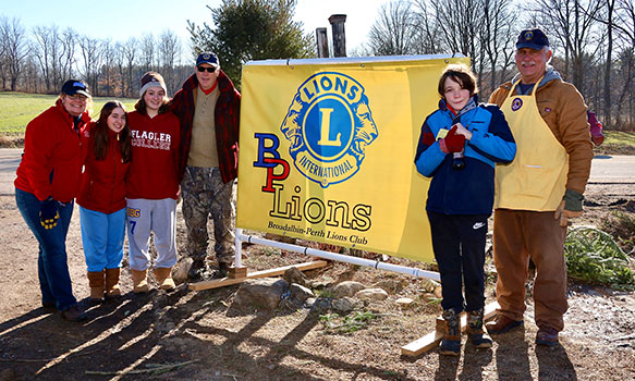 adult and students standing by Lions Club banner