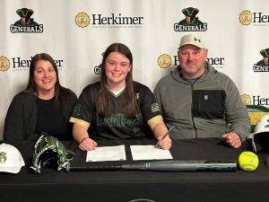 Three people sit at a table while the middle person signs a letter.