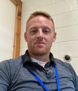 picture of a man with red hair in a dark blue shirt and a lanyard around his neck