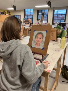 Student with headphones on looks at incomplete portrait.