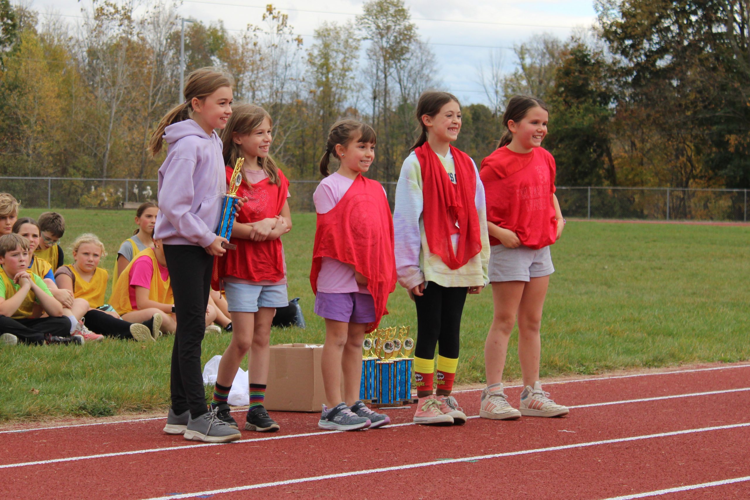 five students stand in a line and smile. one student holds a trophy