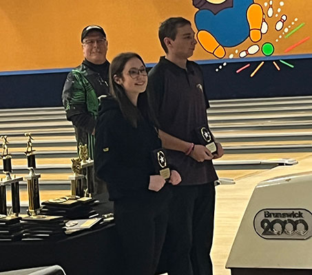 2 bowlers with trophies as adult looks on