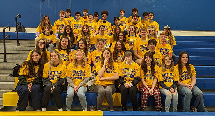 group of students wearing matching t-shirts seated on bleachers