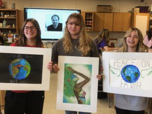 three students hold up their artwork depicting images of peace