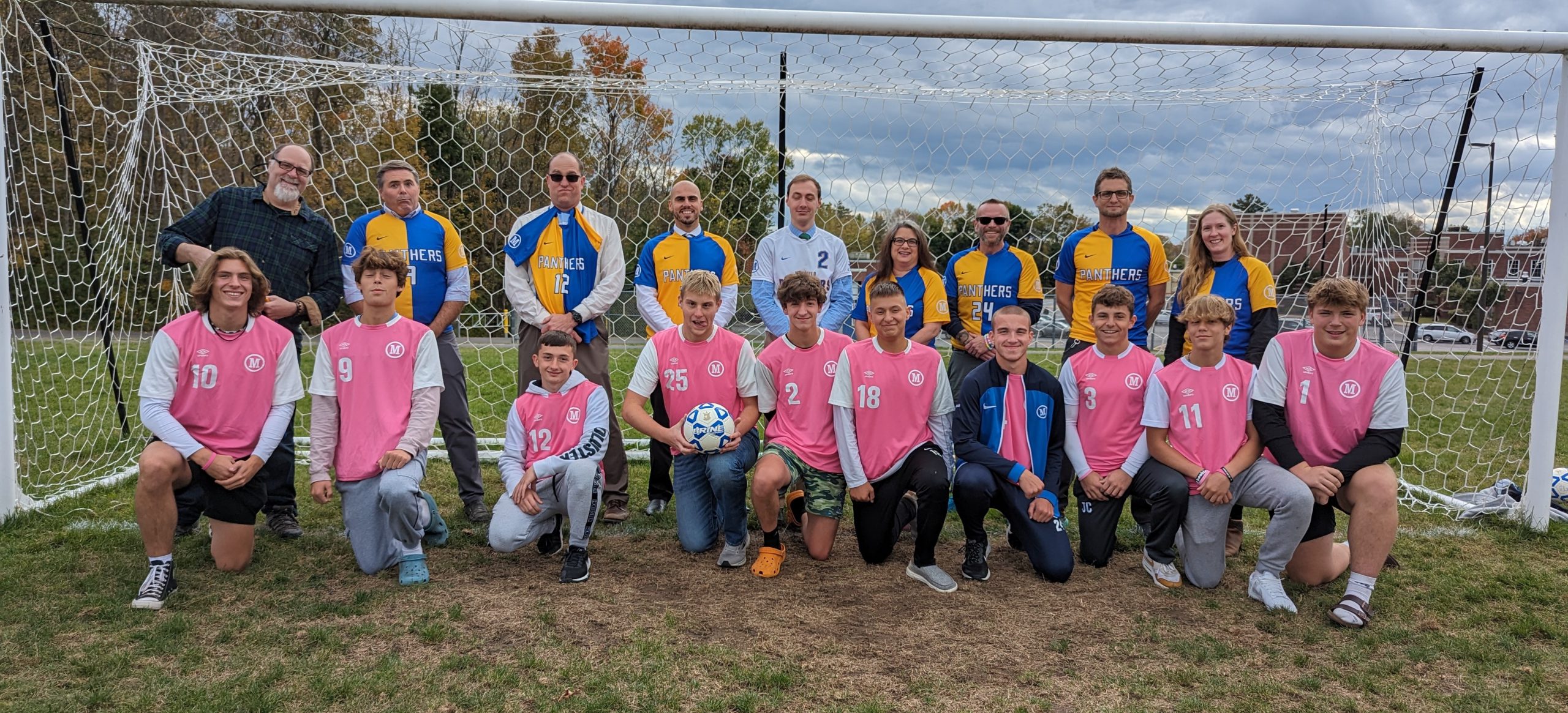 Soccer students and teachers stand in two rows in front of a soccer goal