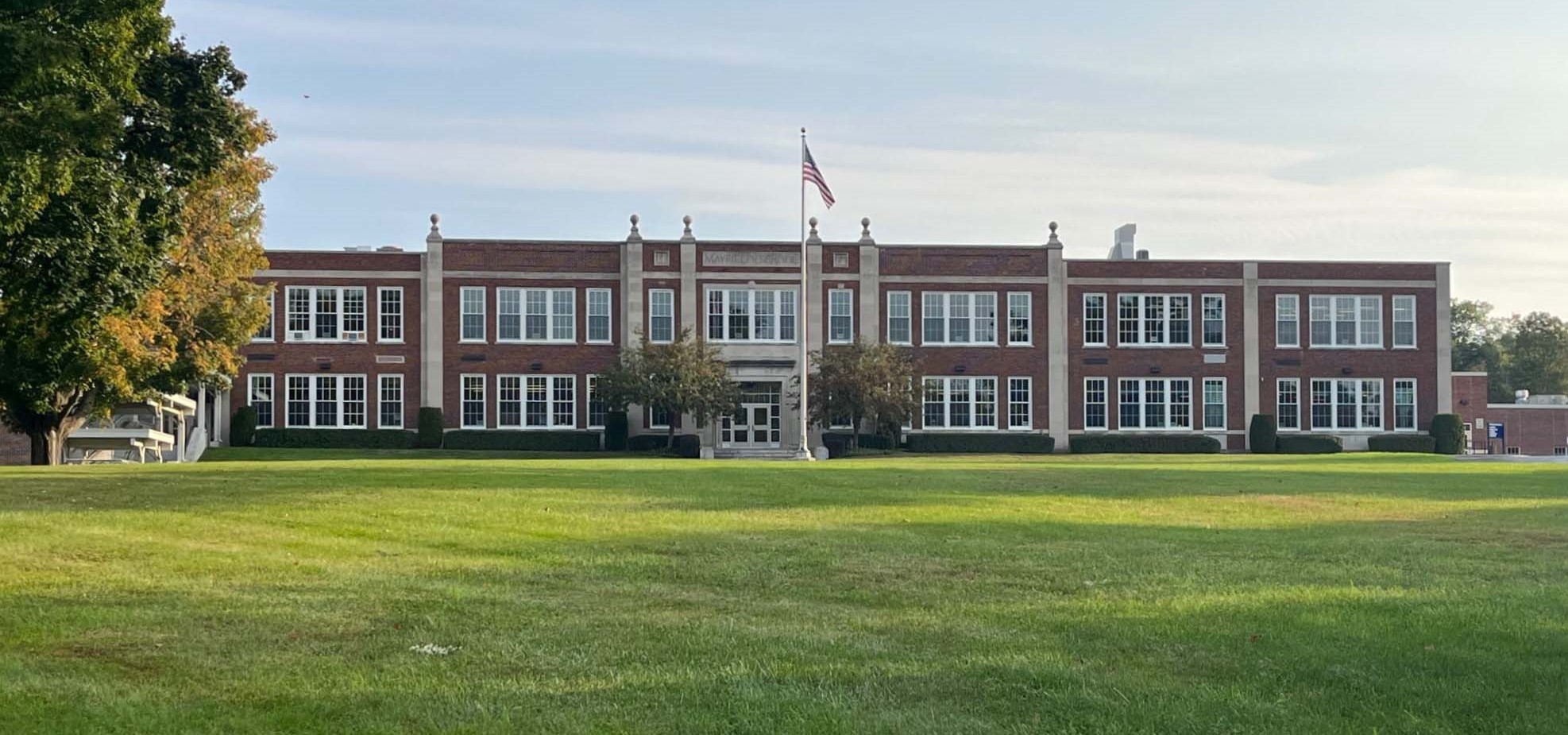 outside of brick school building on a green lawn with an American flag and tree on the left hand side