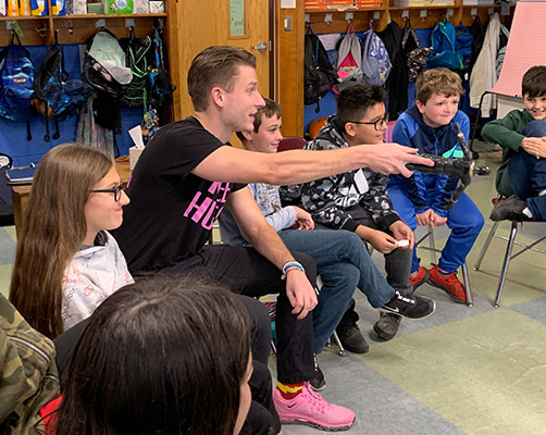 Pat Fish holding doll gestures and talks to a student as other students look on